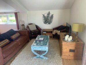 Ein Wohnzimmer mit einem braunen Ledersofa, einem blauen Couchtisch, einem Holznachttisch mit Kerzen und einer Wanddekoration mit Farn.