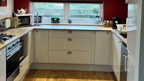 Een moderne keuken met witte kastjes, een magnetron, een waterkoker en een raam met uitzicht op groen.