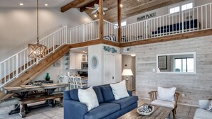 A spacious living area with a blue sofa, wooden coffee table, and a staircase leading to an upper level. - Seascape #311 | 3 BR Corner Condo w/ Loft, Balcony, Gulf Views + Steps to Beach (Orange Beach)