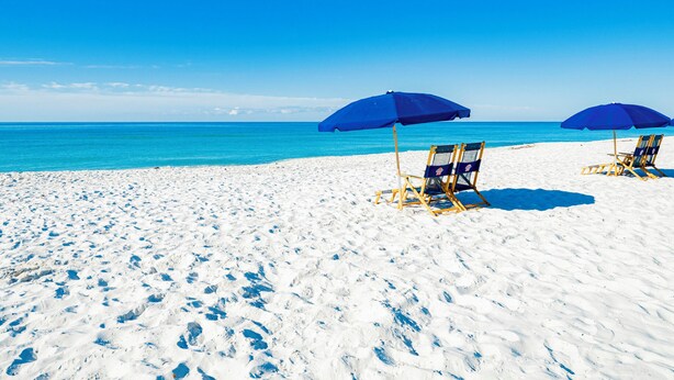 Een strand met twee blauwe parasols en twee strandstoelen.