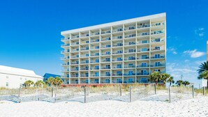 Een hotel met meerdere verdiepingen en balkons, gelegen aan een zandstrand met palmbomen.