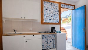 Eine kleine Küche mit Spüle, Herd und Schränken, einer blauen Tür und einem Fenster mit Vorhang mit Fischmuster.