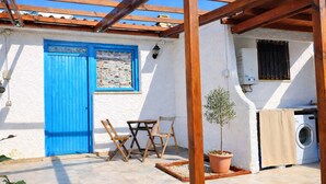 Eine kleine Terrasse im Freien mit einer blauen Tür, Holzmöbeln, einer Waschmaschine und einem Blumentopf mit einem Baum.