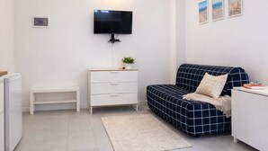 Ein kleines Zimmer mit einem Bett, einem kleinen weißen Schminktisch, einem an der Wand befestigten Fernseher und einem kleinen Regal.