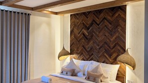 Ein modernes Schlafzimmer mit Holzboden, einer Wand mit Fischgrätenmuster, einem Bett mit beiger Bettdecke, zwei Nachttischlampen und einem Nachttisch aus Holz.