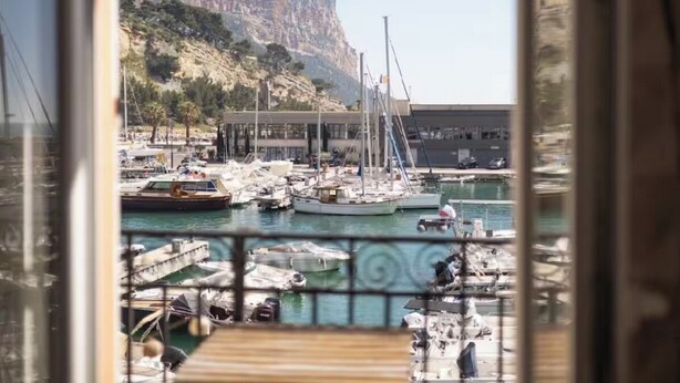 A marina with boats, a cliff, and a building in the background. - L'échappée Mer (Cassis)