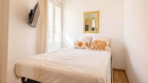 A bedroom with a bed, a window, a wall-mounted mirror, and a wall-mounted device. - L'échappée Mer (Cassis)