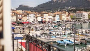 A marina with boats docked, a mountainous backdrop, and buildings with balconies. - L'échappée Mer (Cassis)