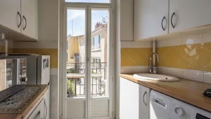 A compact kitchen with a washing machine, a sink, and a view of a balcony. - L'échappée Mer (Cassis)
