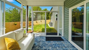 A sunlit room with a white sofa, a yellow pillow, and a view of a backyard through glass doors. - SoKno Retreat, Pool Table, Sunroom, 15 min-Knox, 35-Sevier (Knoxville)