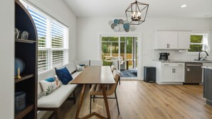 A modern kitchen with white cabinets, a dining area with a bench and table, and a view through a glass door to an outdoor space. - SoKno Retreat, Pool Table, Sunroom, 15 min-Knox, 35-Sevier (Knoxville)