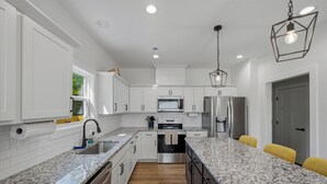 A modern kitchen with white cabinetry, granite countertops, stainless steel appliances, and a central island with seating. - SoKno Retreat, Pool Table, Sunroom, 15 min-Knox, 35-Sevier (Knoxville)