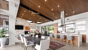 Uma cozinha moderna com uma ilha central, uma área de jantar com uma mesa grande e uma parede decorada com pedra.