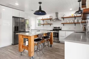 Una cocina moderna con armarios blancos, un refrigerador de acero inoxidable, una isla de madera con taburetes altos e iluminación colgante.