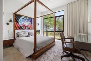 A bedroom with a four-poster bed, a desk with a chair, a large window, and a painting on the wall. - Luxury 26-Acre Compound, w/ Pool & Amazing Views (Wimberley)
