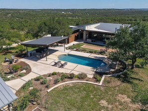 A modern house with a swimming pool, covered patio, and a view of the surrounding landscape. - Luxury 26-Acre Compound, w/ Pool & Amazing Views (Wimberley)