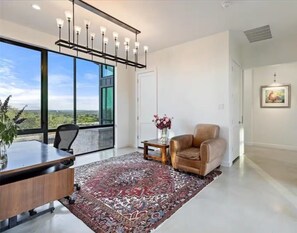 A modern office space with a large desk, a leather chair, a patterned rug, and a view through large windows. - Luxury 26-Acre Compound, w/ Pool & Amazing Views (Wimberley)