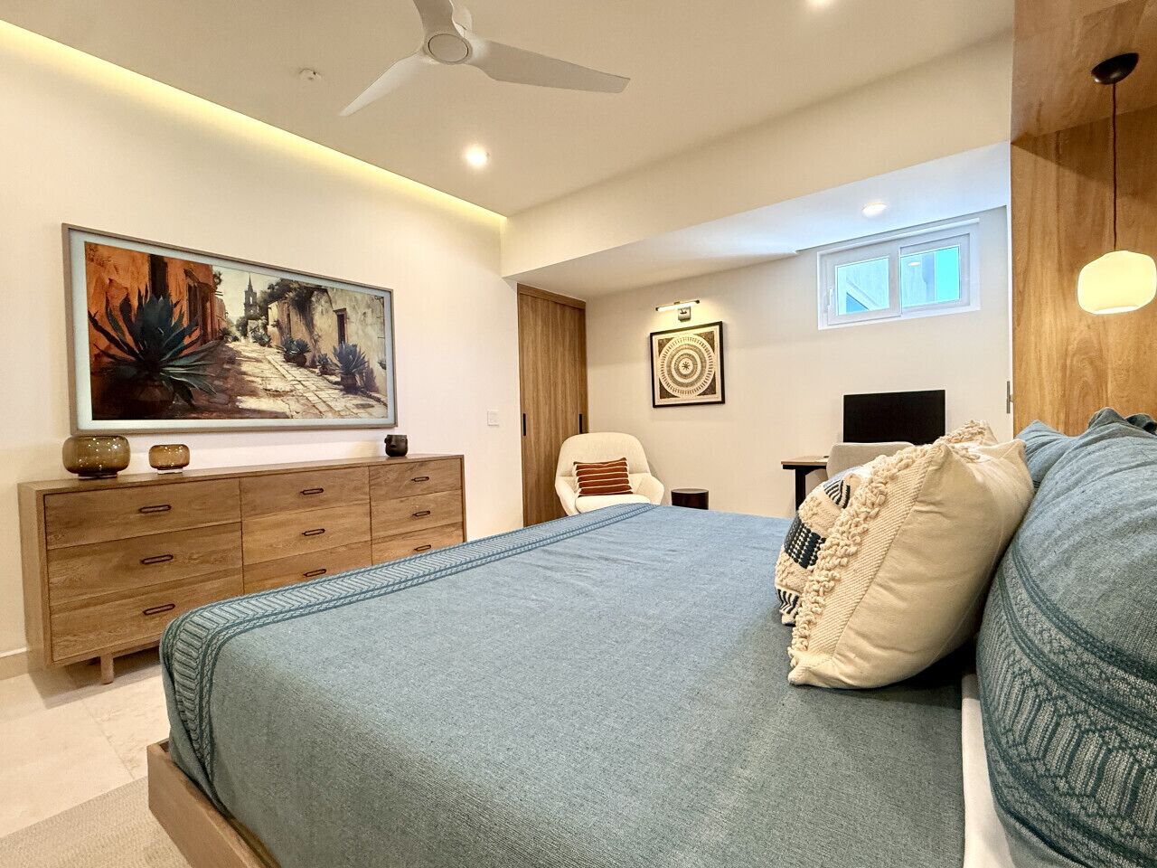 Une chambre à coucher comprenant un lit, une commode, une chaise, un tableau et un ventilateur de plafond.