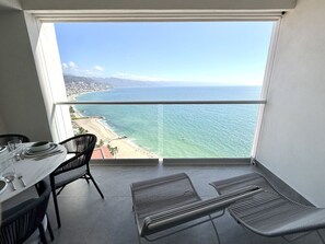 A balcony with a view of the ocean and a beach, furnished with a table and chairs. - Harbor 171 Unit 2209 – High-Floor Oceanview 1BR XL with Rooftop Pool (Puerto Vallarta)