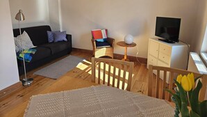 Olohuoneessa on sohva, televisio, pieni pöytä, jossa on lamppu, ja tuoli.