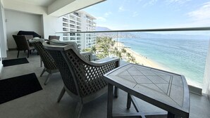 A balcony with a table and chairs, overlooking a beach and cityscape. - Harbor 171 – Oceanview Condo + Rooftop Pool (28th Floor) (Puerto Vallarta)