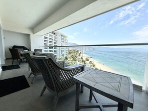 A balcony with a table and chairs, overlooking a beach and cityscape. - Harbor 171 – Oceanview Condo + Rooftop Pool (28th Floor) (Puerto Vallarta)