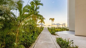 A pathway lined with palm trees leading to a building with a view of the sunset. - Harbor 171 – Oceanview Condo + Rooftop Pool (28th Floor) (Puerto Vallarta)