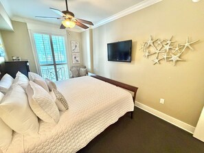 Habitación de hotel con cama, ventilador de techo, televisor y estrellas de mar decorativas en la pared.