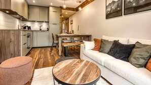 A modern living room with a white sofa, round wooden coffee table, and a pink ottoman. - Appart 5pax | Parking | Balconies | Views (Chamonix-Mont-Blanc)