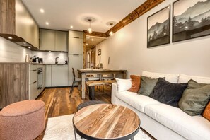 A modern living room with a white sofa, round wooden coffee table, and a pink ottoman. - Appart 5pax | Parking | Balconies | Views (Chamonix-Mont-Blanc)