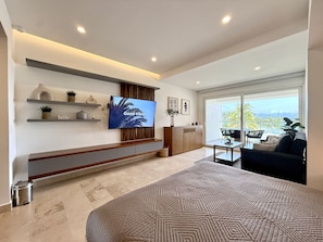 A modern bedroom with a large bed, a TV mounted on the wall, a small table, and a sofa. - Harbor NT208 by Moikkarentals (Puerto Vallarta)