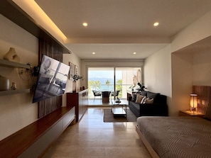 A modern hotel room with a large TV, a sofa, a bed, a dining area, and a balcony with a view. - Harbor NT208 by Moikkarentals (Puerto Vallarta)