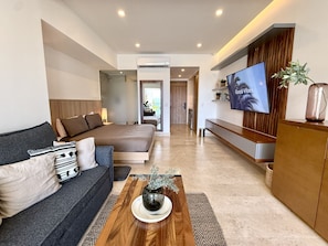 A modern living room with a sofa, coffee table, TV, and a bed. - Harbor NT208 by Moikkarentals (Puerto Vallarta)