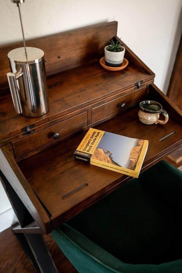 Un escritorio de madera con un libro, una taza y una pequeña planta en maceta.