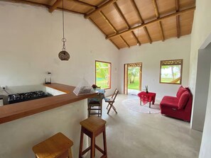A spacious living area with a red sofa, a kitchen with a gas stove, and large windows offering views of greenery. - House on Caraíva Beach (Caraíva)