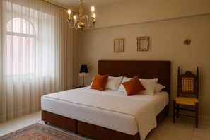Ein Hotelzimmer mit einem großen Bett, einer Kandelaber, einem Nachttisch mit Lampe und einem Sessel.