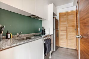 Eine Küche mit weißen Schränken, einer grünen Spritzschutzwand, einer Spüle aus Edelstahl und einer Holztür.