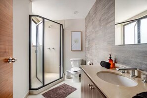 A modern bathroom with a glass shower enclosure, a toilet, a sink with a mirror, and a framed picture on the wall. - 205-2 3 BR 2 Baths Private Terrace - Roma Norte (Mexico City)