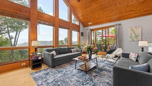 A spacious living room with large windows, a gray sofa, a coffee table, and a view of the outdoors. - 1st in Sugar/View/EV Charge/Hot Tub/Sauna/Pet Friendly/Sleeps 12/Two Master Bdrs (Sugar Mountain)