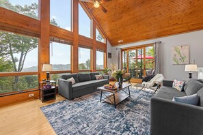A spacious living room with large windows, a gray sofa, a coffee table, and a view of the outdoors. - 1st in Sugar/View/EV Charge/Hot Tub/Sauna/Pet Friendly/Sleeps 12/Two Master Bdrs (Sugar Mountain)