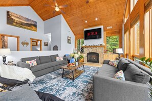 A living room with a fireplace, a television mounted on the wall, and a ceiling fan. - 1st in Sugar/View/EV Charge/Hot Tub/Sauna/Pet Friendly/Sleeps 12/Two Master Bdrs (Sugar Mountain)