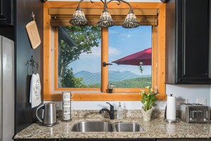A kitchen with a granite countertop, stainless steel sink, a coffee pot, a toaster, and a window with a view of mountains. - 1st in Sugar/View/EV Charge/Hot Tub/Sauna/Pet Friendly/Sleeps 12/Two Master Bdrs (Sugar Mountain)