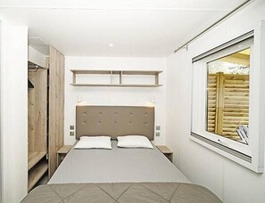 A bedroom with a bed, bedside tables, a window, and a built-in wardrobe. - Spacious Adriatic Family Mobile Home (Brtonigla)