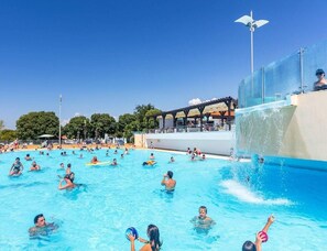 Uma piscina com pessoas, um toboágua e um edifício com área coberta ao fundo.