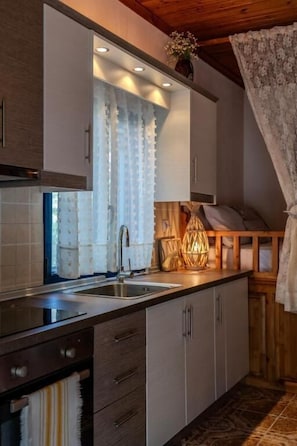 A modern kitchen with a built-in oven, a stainless steel sink, and wooden cabinets. - Irene's Cottage Myrtonas (Karpathos)