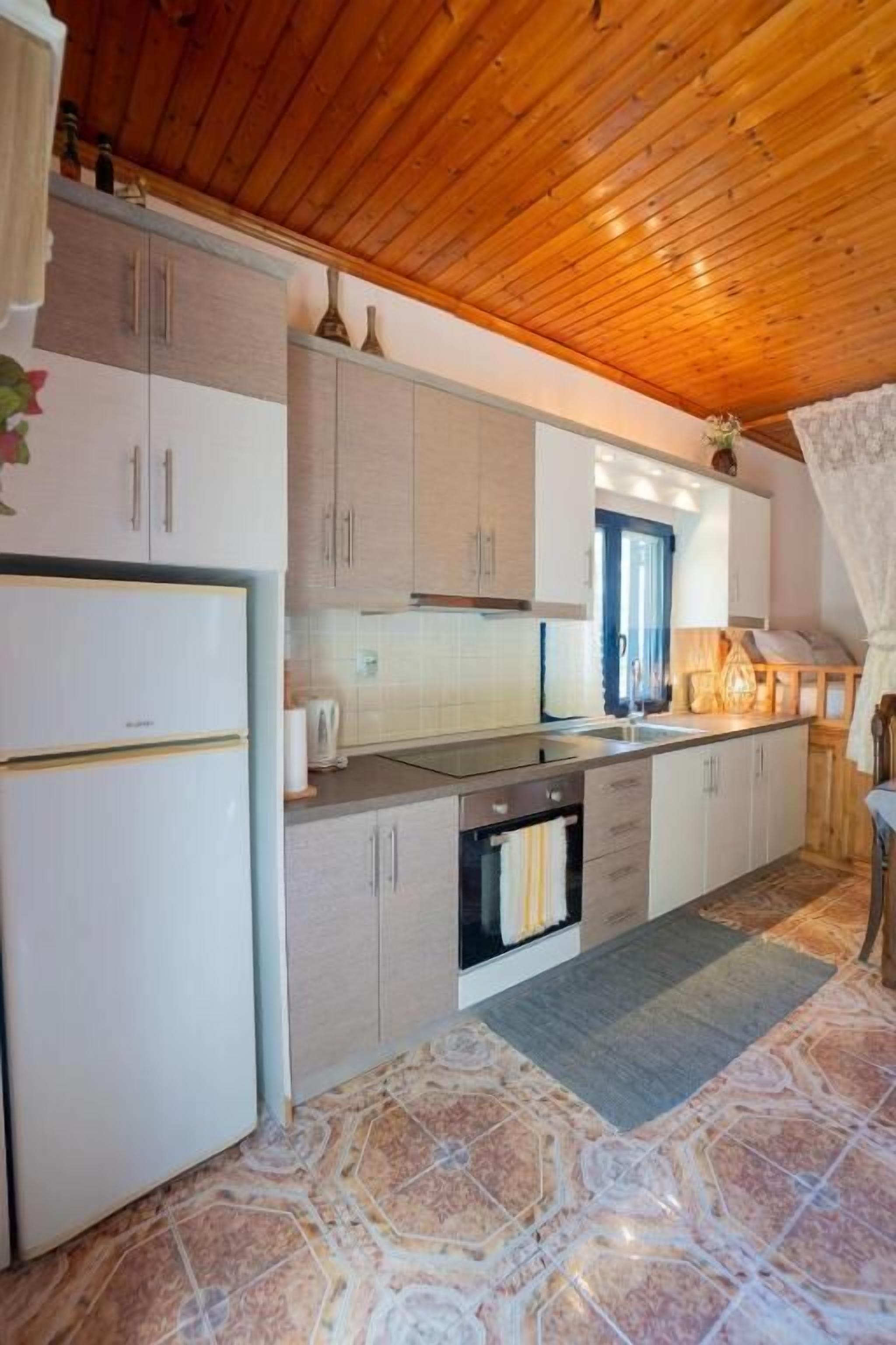 A kitchen with wooden ceiling, white cabinets, a stove, and a sink.