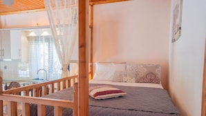 A bedroom with a wooden bed frame, a canopy, and a view of a kitchen and bathroom. - Irene's Cottage Myrtonas (Karpathos)