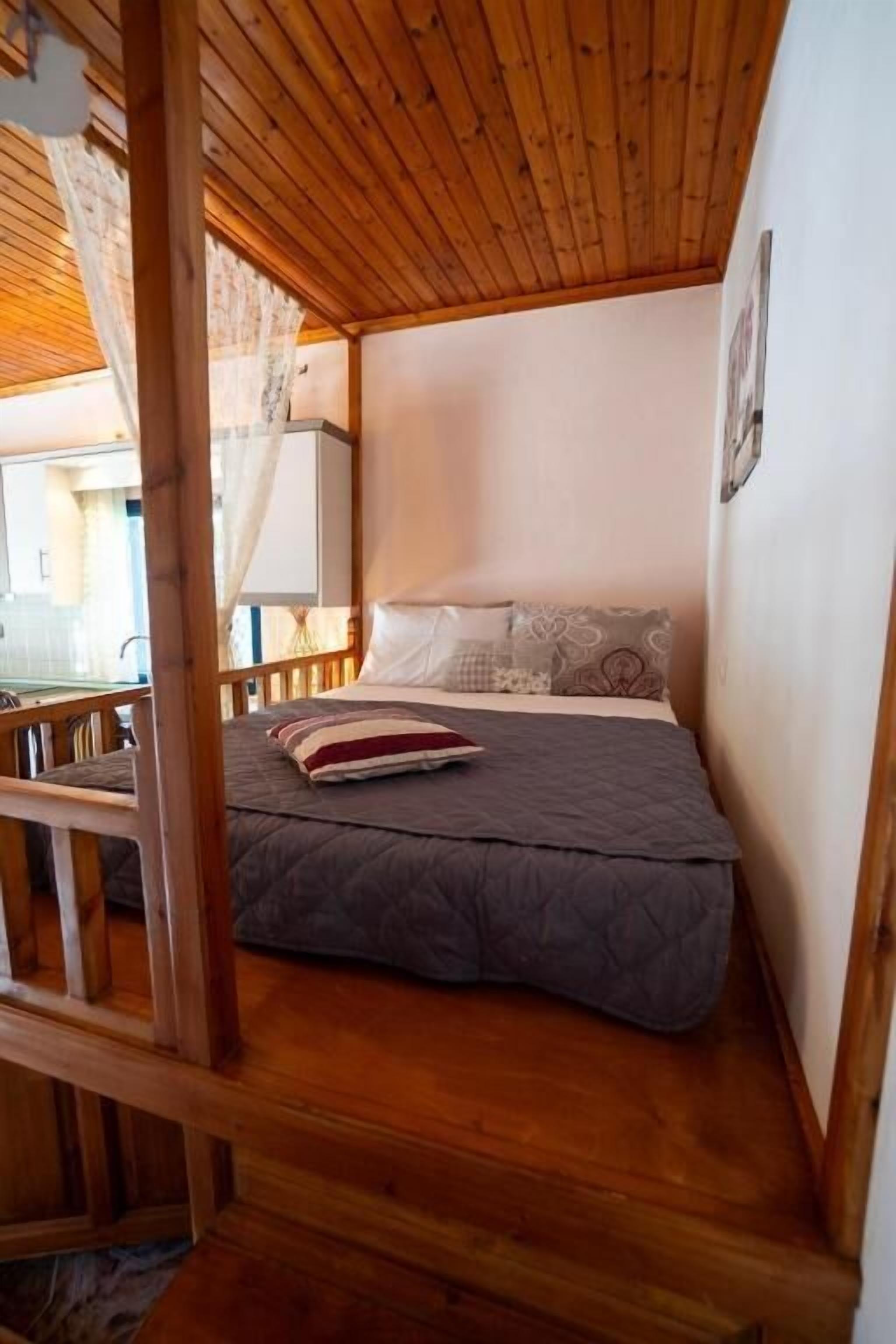 Un dormitorio pequeño y acogedor con techo de madera, cama con colcha gris y una silla de madera.