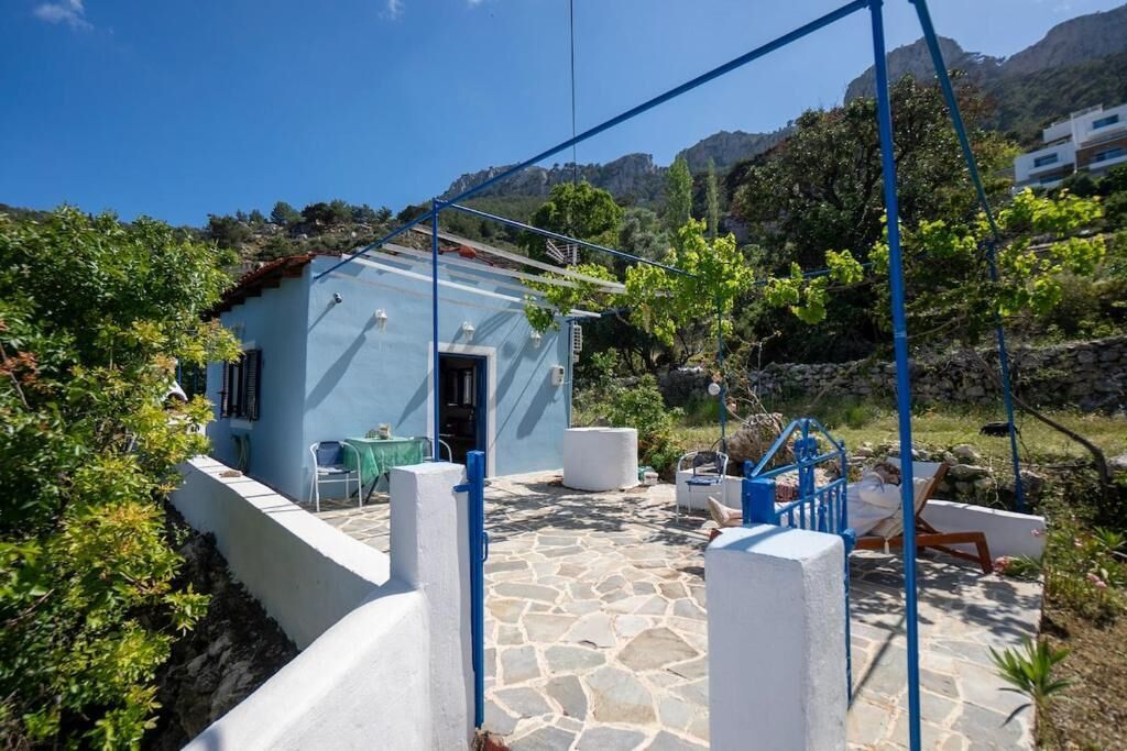 Un bâtiment de couleur bleu clair doté d’une terrasse en pierre, d’un espace extérieur aménagé pour s’asseoir et offrant une vue sur le paysage environnant.