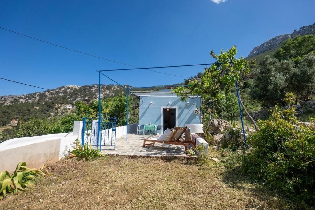 A small, light blue building with a patio, a table, and a chair.